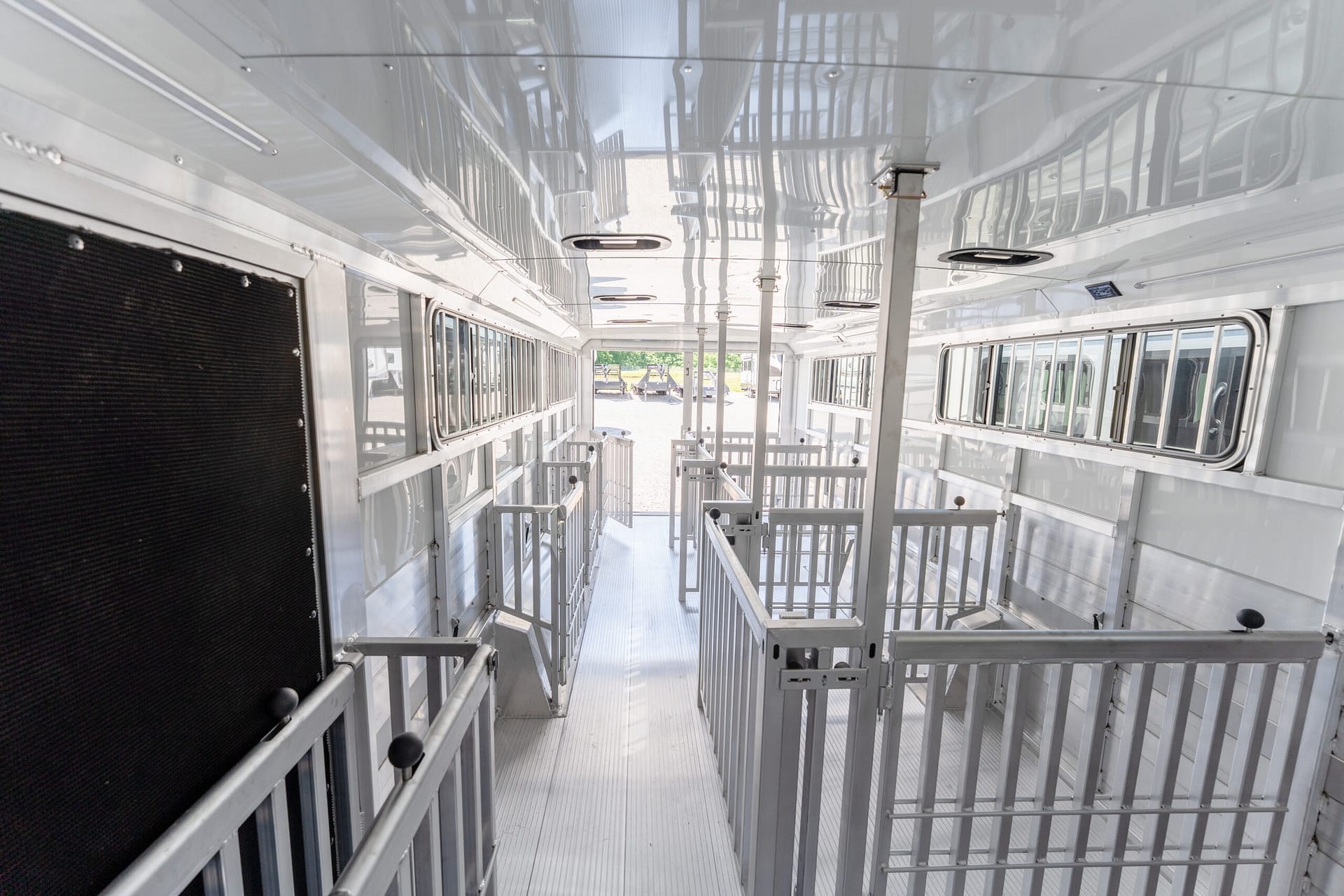 Interior of a silver livestock trailer with metal rails and a narrow walkway toward the back, stalls on both sides.