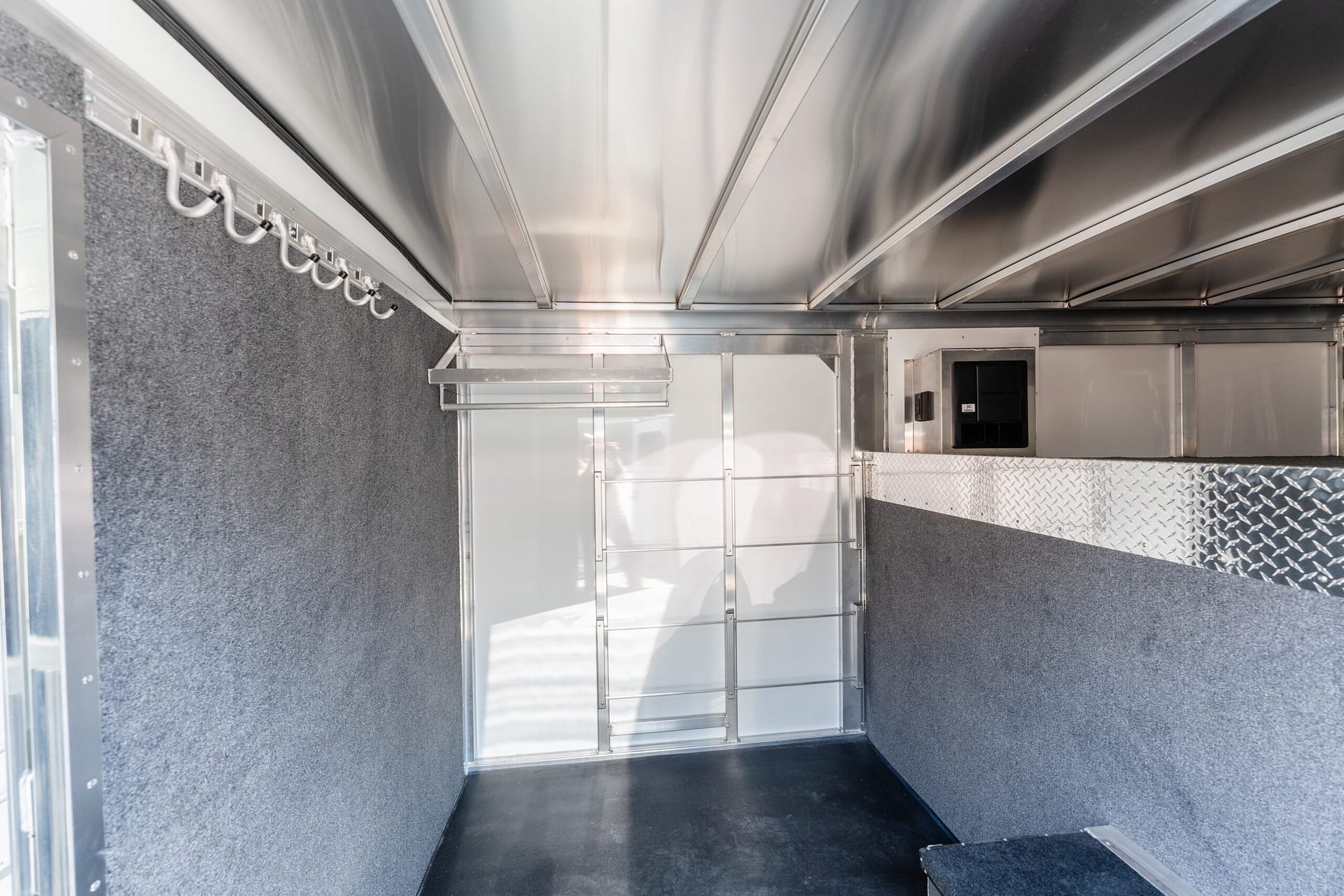 Interior of a metal utility trailer with aluminum walls, hooks along the left wall, and a diamond-plate step on the right.