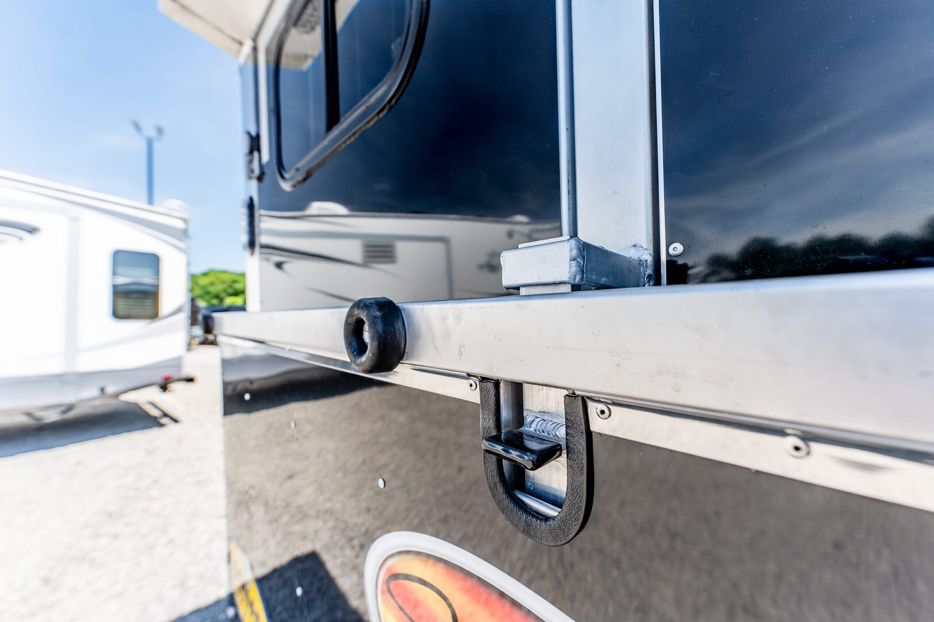 Close-up of a trailer hitch and black bumper on a glossy trailer, outdoors in a parking lot.