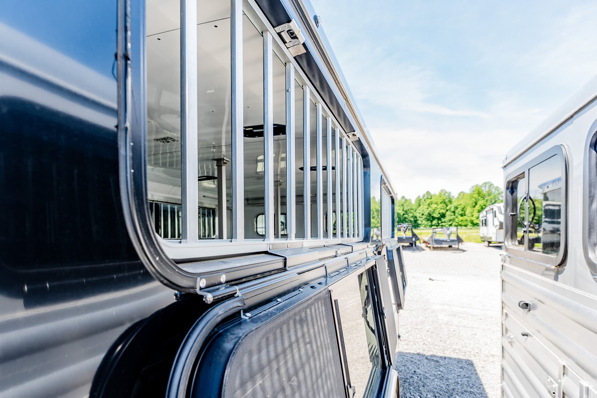 Close-up of a black livestock trailer with vertical metal bars along the side, parked beside another trailer on a sunny day.