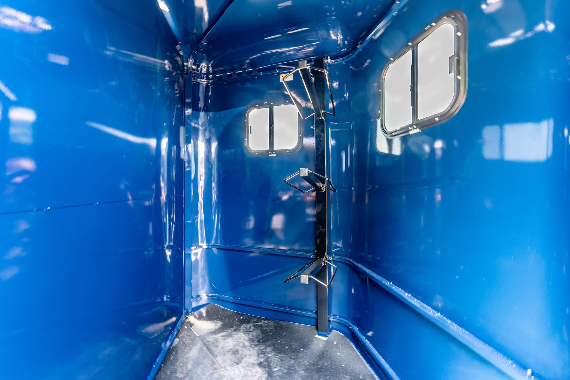 Narrow blue metal interior with glossy walls, small rounded windows and exposed brackets along the ceiling.