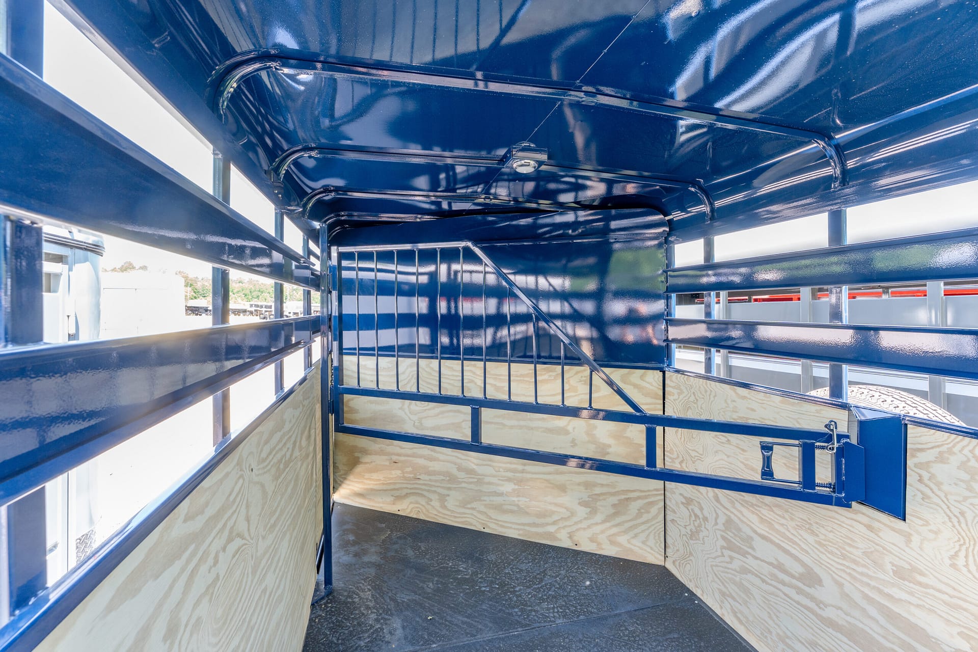 Blue-painted metal trailer interior with railing and plywood walls, into-lighted open cargo area outside visible through gaps