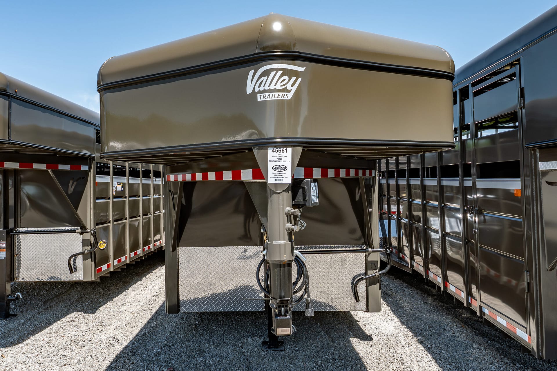 Front view of a Valley Trailers gooseneck trailer with hitch, tan body, and reflective diamond-plate panels under bright sky.