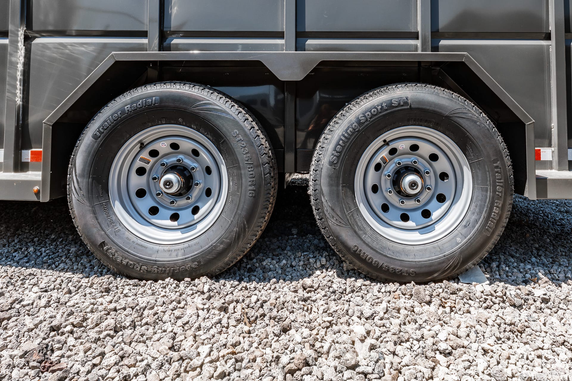 Close-up of two trailer wheels on a dark trailer, resting on gravel ground.