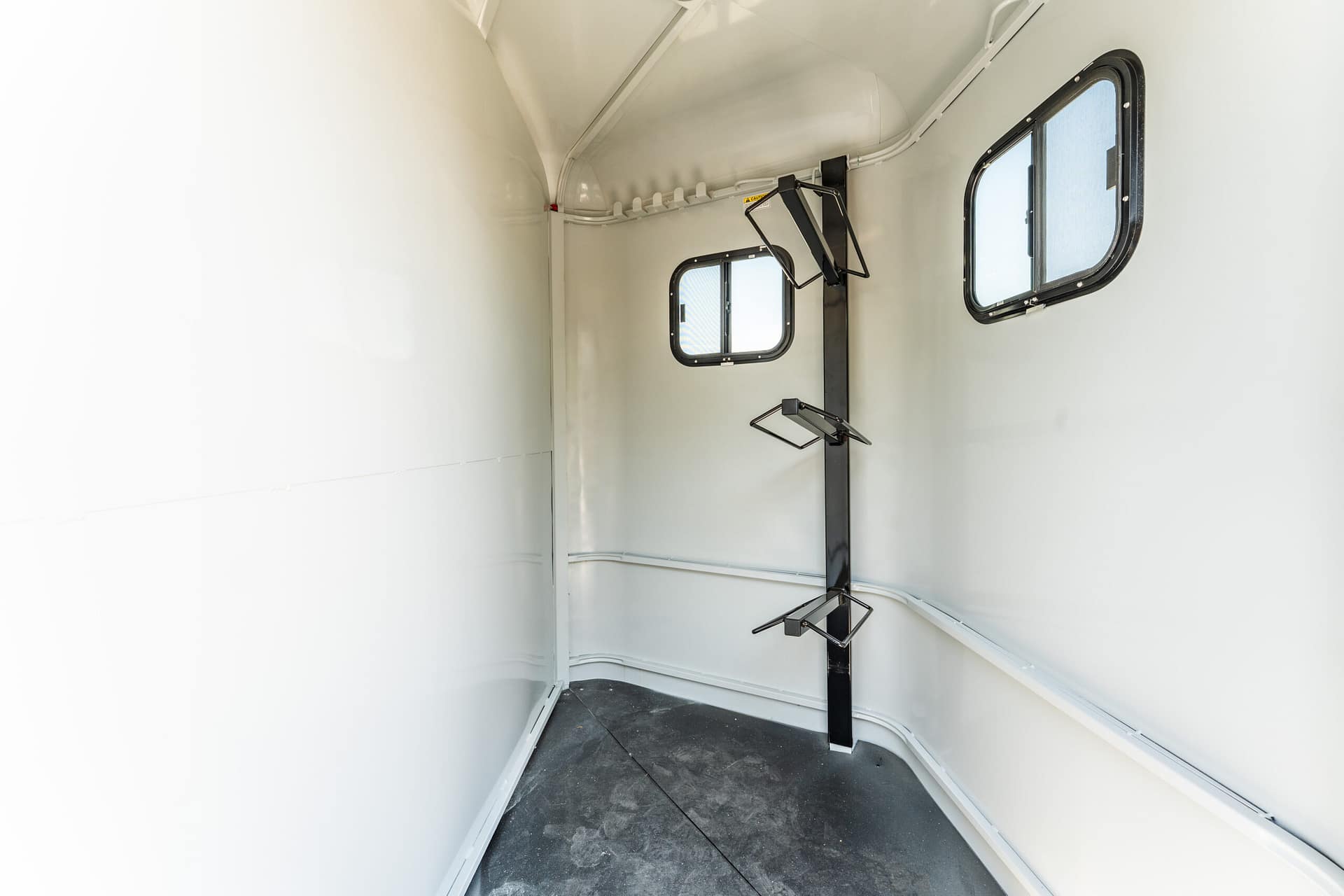 Interior of a small empty trailer or cargo area with a vertical support post and fold-down racks near two small rectangular windows on the right side.