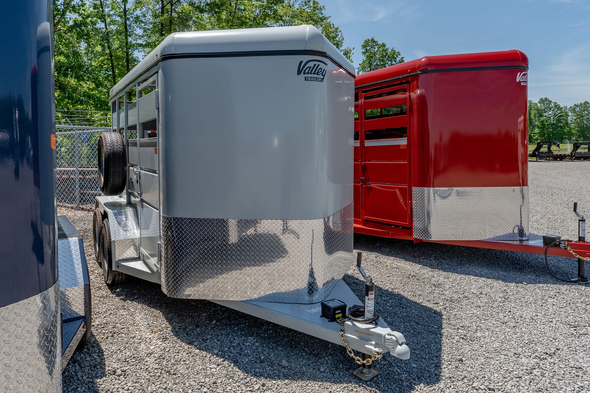 Close-up of a silver trailer hitch with safety chains on a gravel lot, next to a red trailer