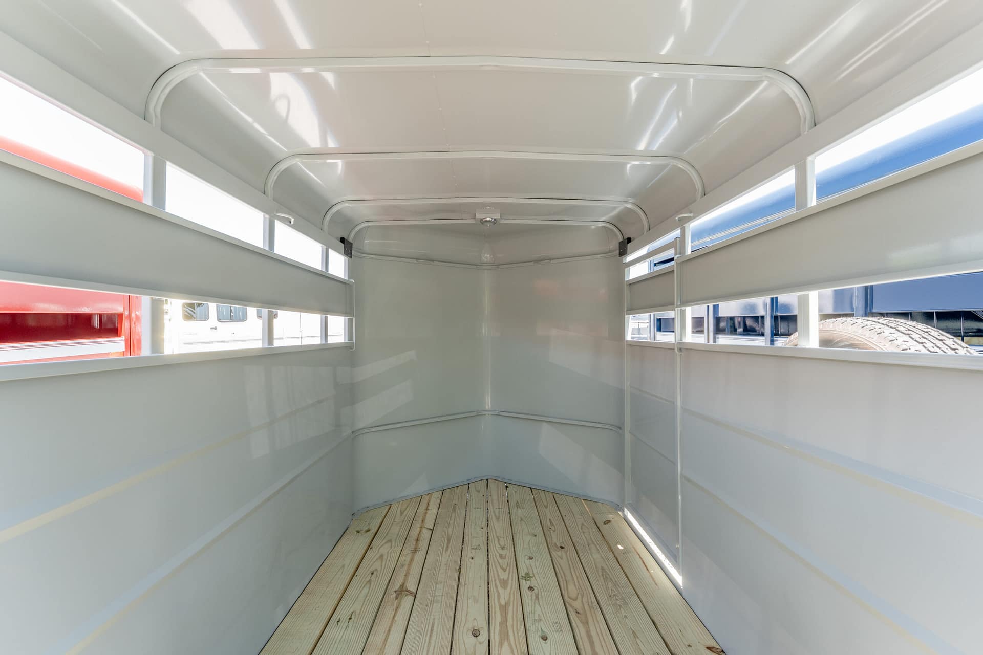 Empty light-gray metal trailer interior with a wooden plank floor and side rails outside.