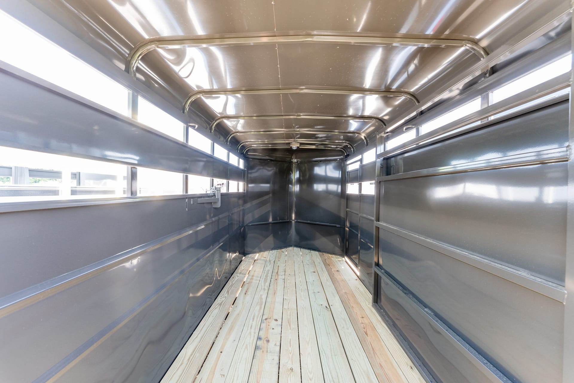 Interior of an empty aluminum trailer with a wooden floor and side windows.