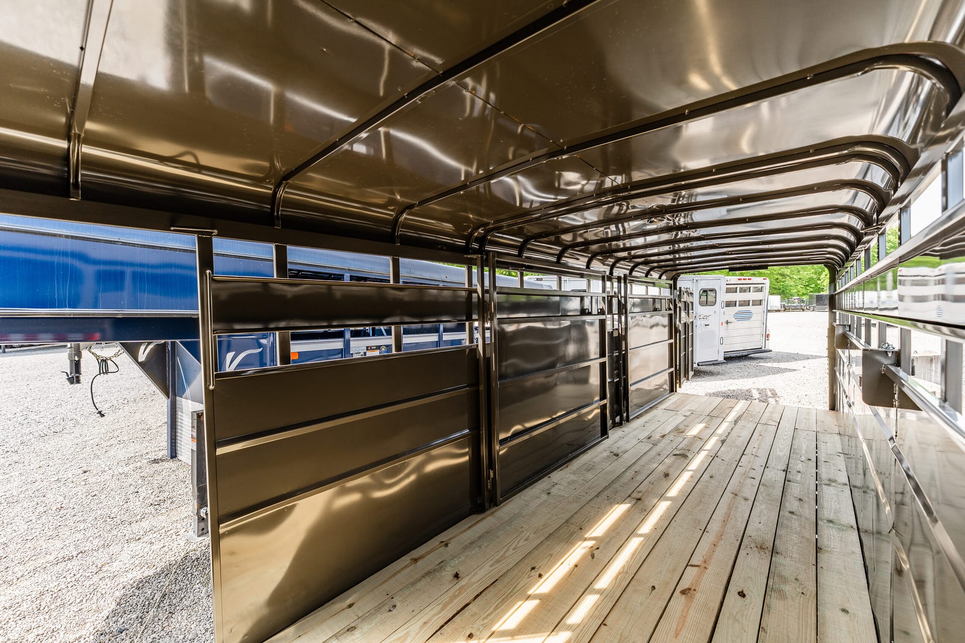 Interior of a shiny aluminum livestock trailer with side stalls and a wooden floor
