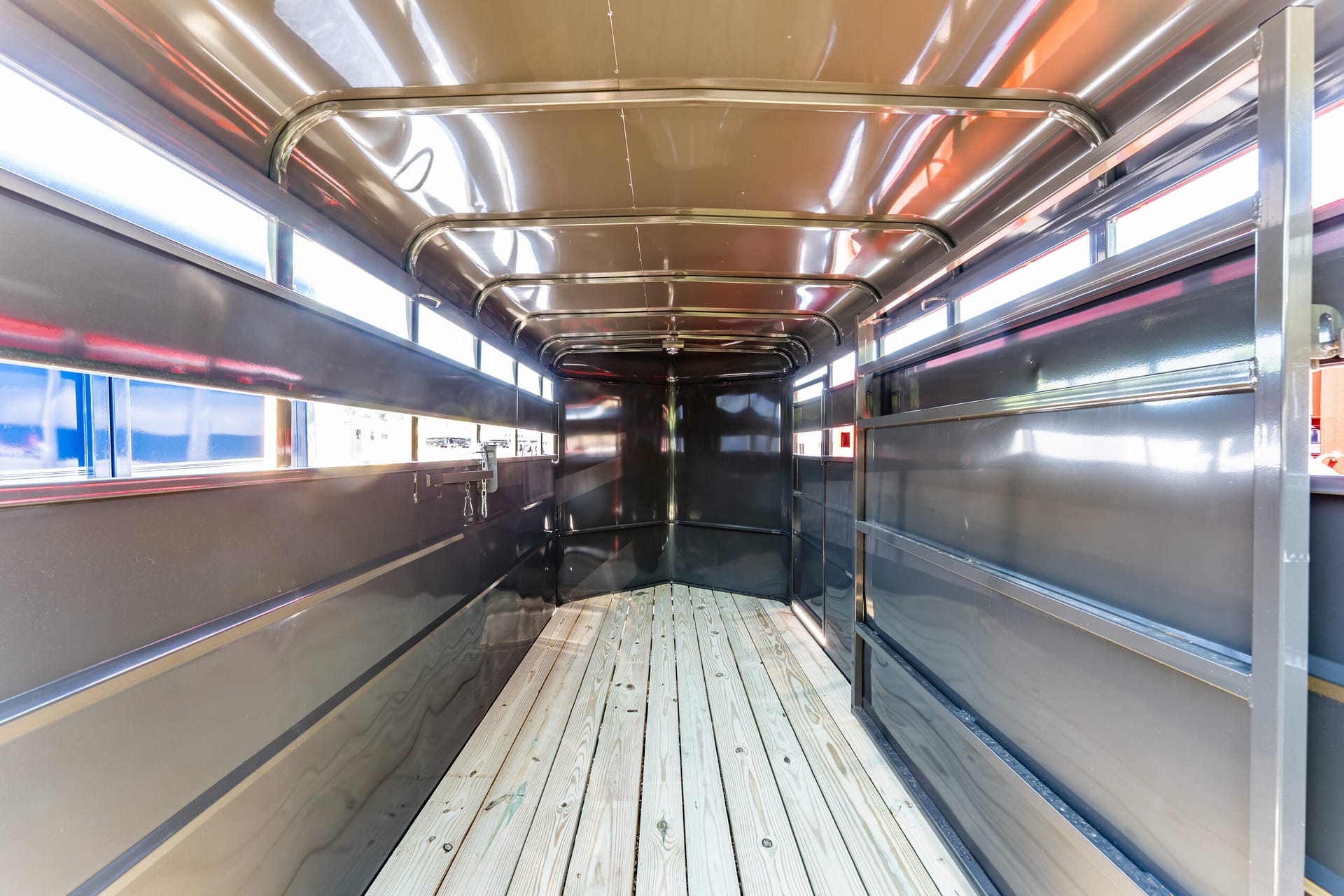 Interior of an empty metal cargo trailer with wooden plank floor and shiny reflective walls and ceiling