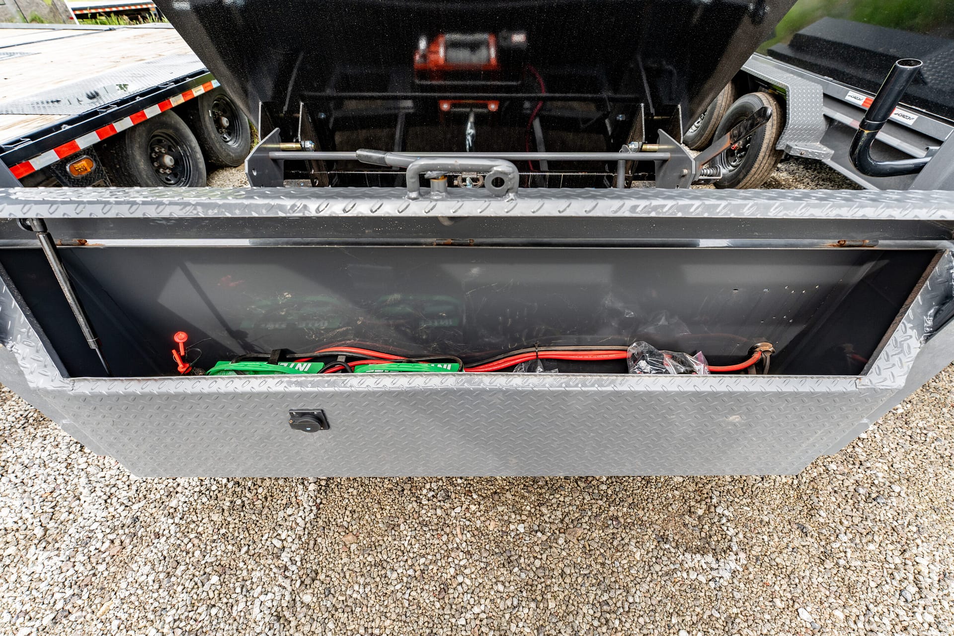 Open diamond-plate metal toolbox on a trailer, exposing red and black battery cables and miscellaneous wiring inside.