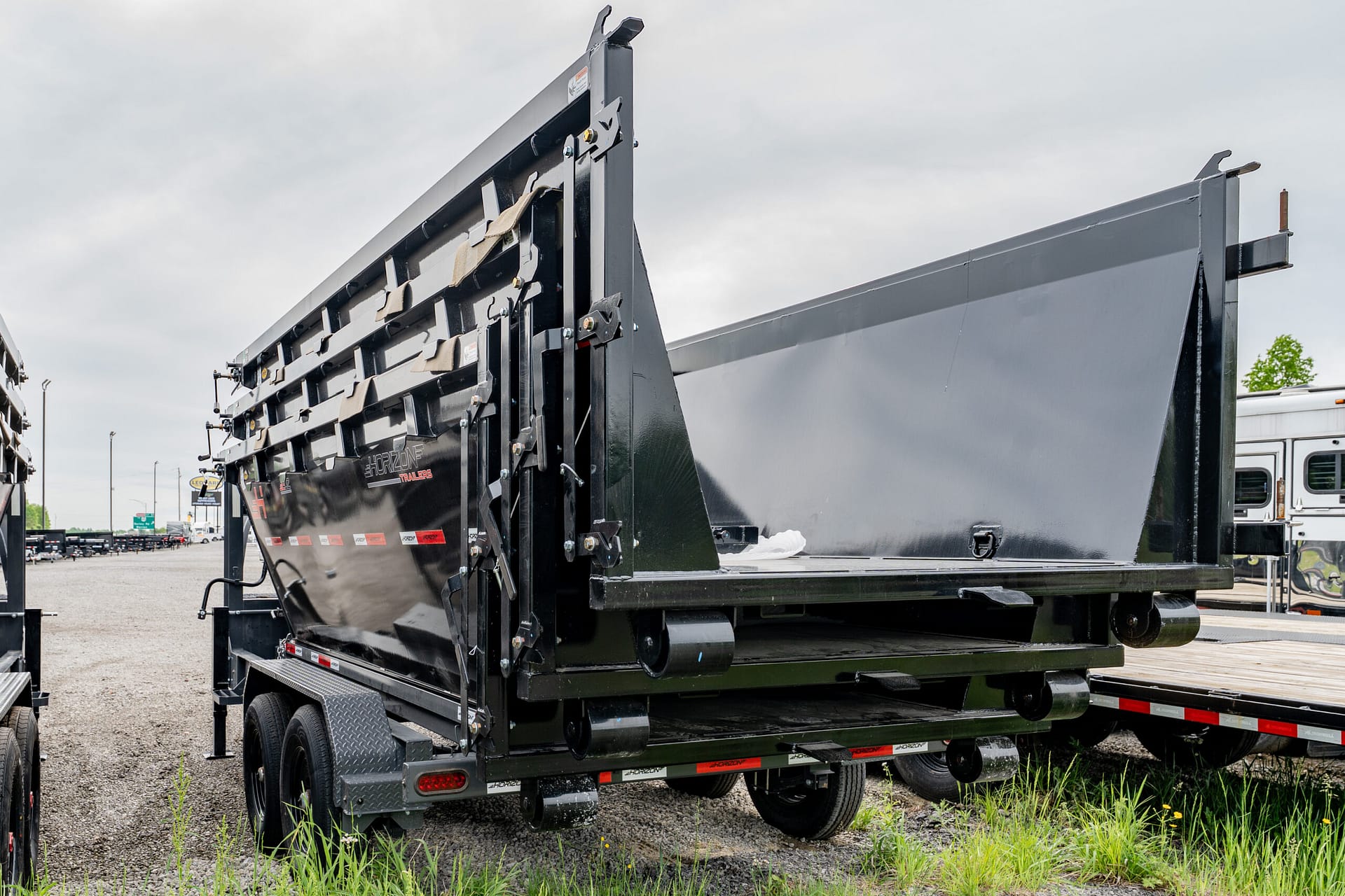 Close-up of a black Horizon dump trailer with reinforced side walls on a gravel lot.