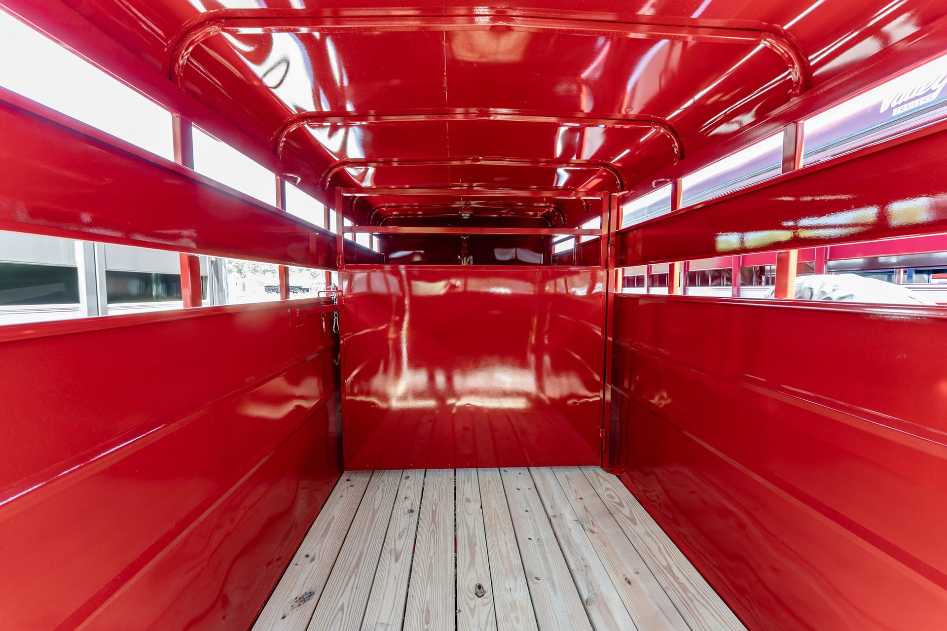 Inside a red metal trailer with glossy walls and a wooden plank floor, viewed from the rear.