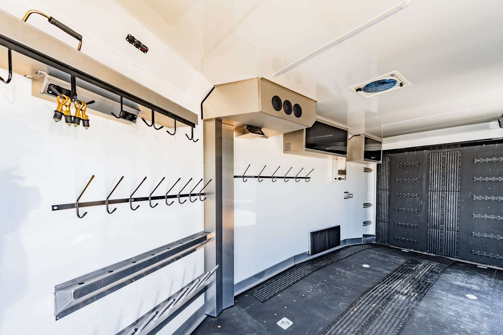 Interior of a white utility trailer with overhead stainless vent and rows of hooks along the wall for hanging tools.