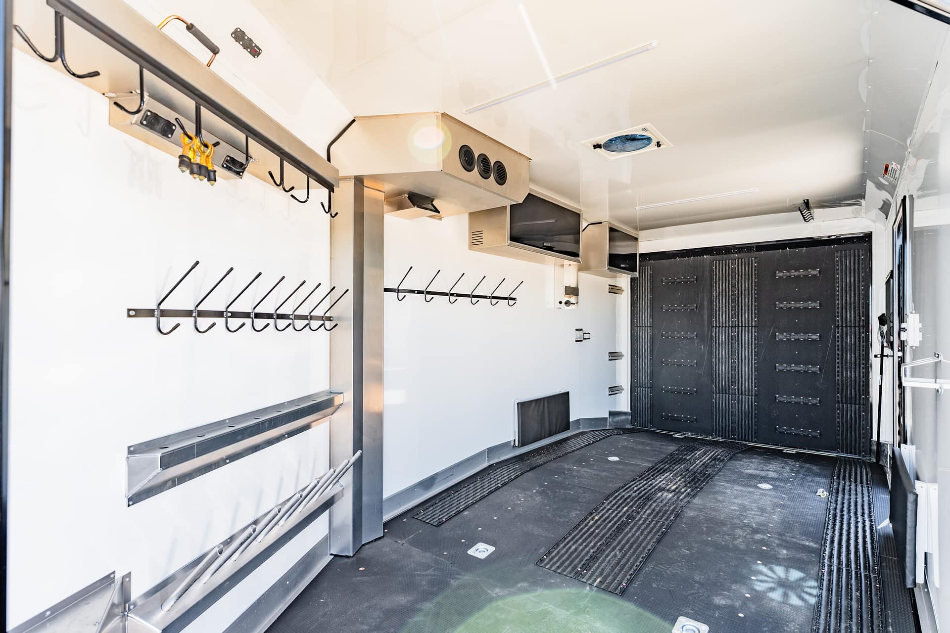 Interior of a stainless-steel utility trailer with hooks, racks, and ventilation vents along white walls.”,