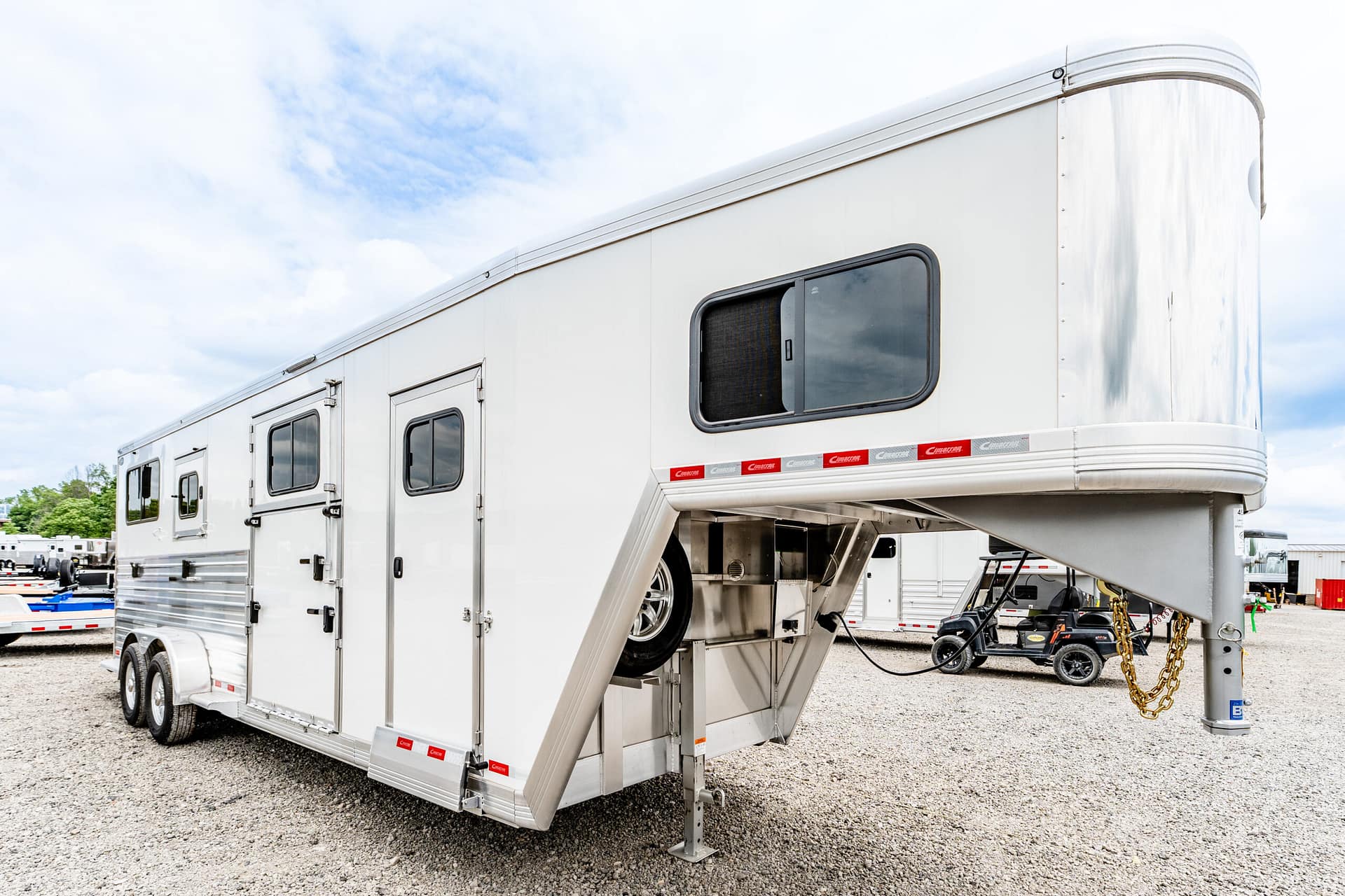 White large travel trailer with living quarters, side window, and a lowered ramp/stairs in a gravel lot with other trailers nearby