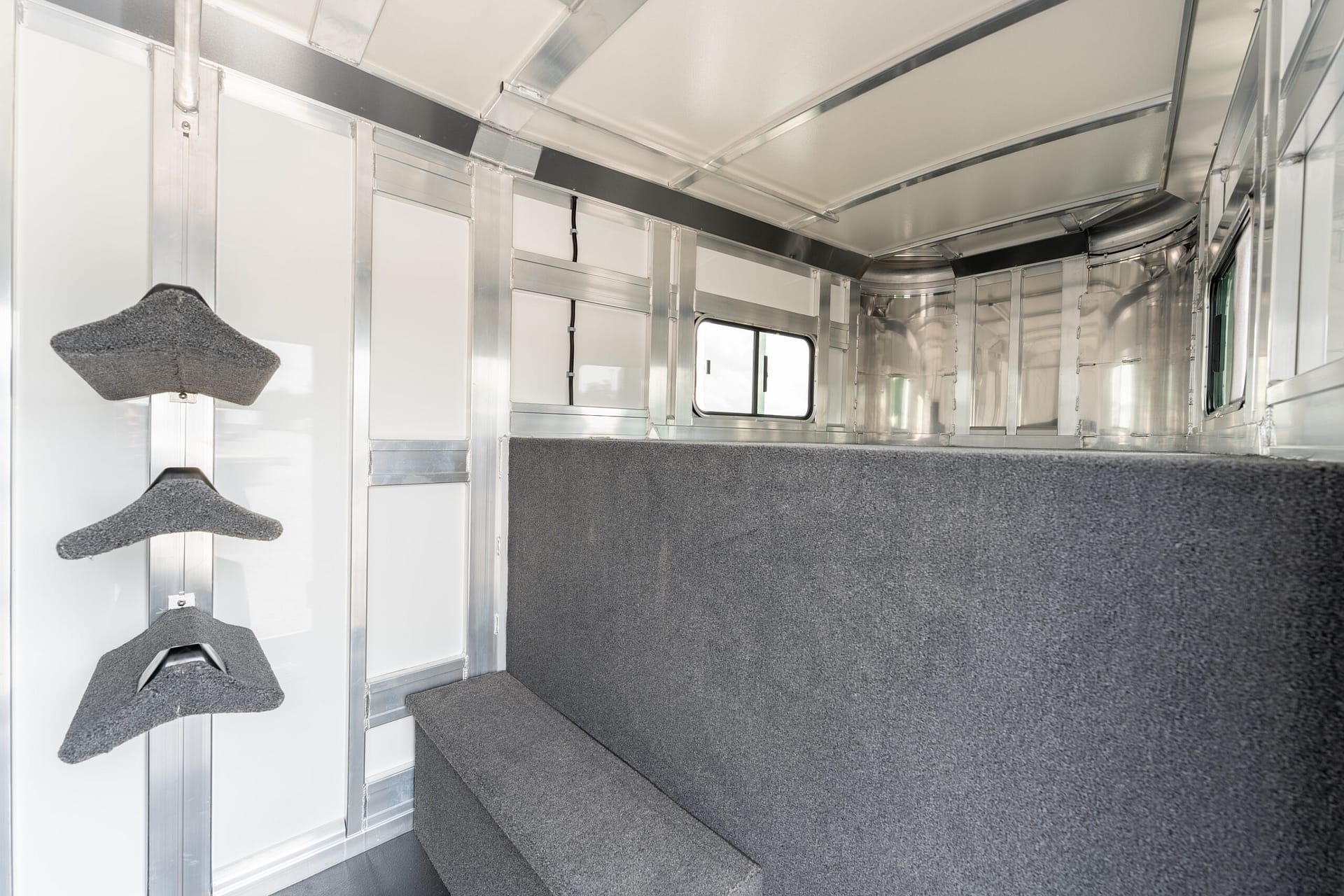 Interior of a metal-walled trailer or mobile unit with white panels, exposed framing, and gray carpeted steps along the left side.