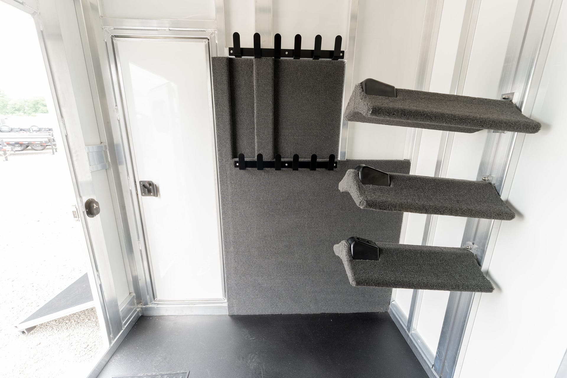 Interior of a metal trailer with grey carpeted steps and foam padding, leading to a doorway on the left.