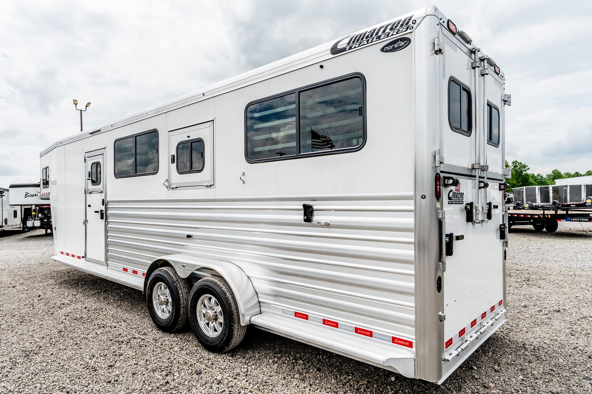 Large white travel trailer with living-quarters style design, windows, and dual-axle wheels parked on a gravel lot.
