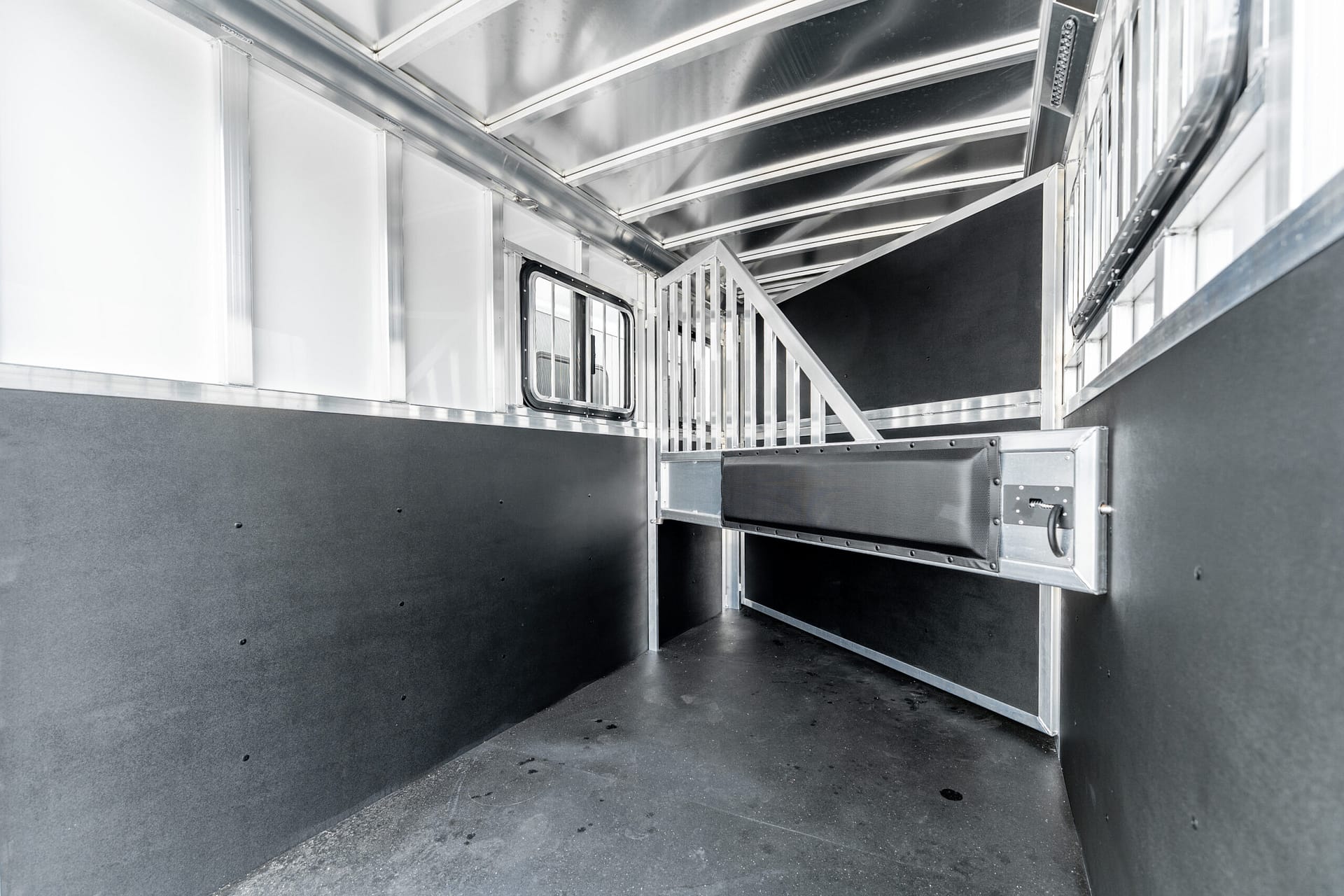 Interior of a silver metal trailer with ribbed walls, a small window, and a raised metal staircase at the far end, empty cargo space behind.