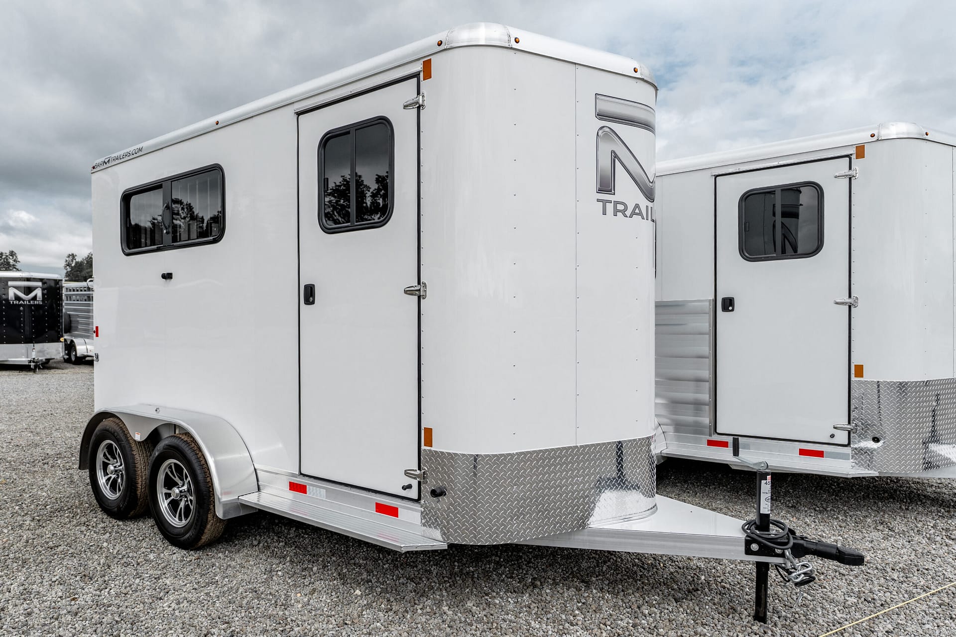 White cargo trailer with diamond-plate front, hitch and support jack on gravel lot, two trailers in background
