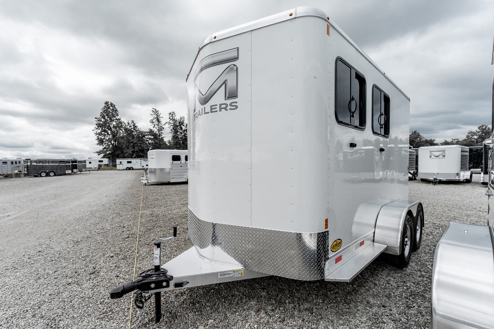 White travel trailer with metal diamond-plate front, parked on a gravel lot under a cloudy sky.