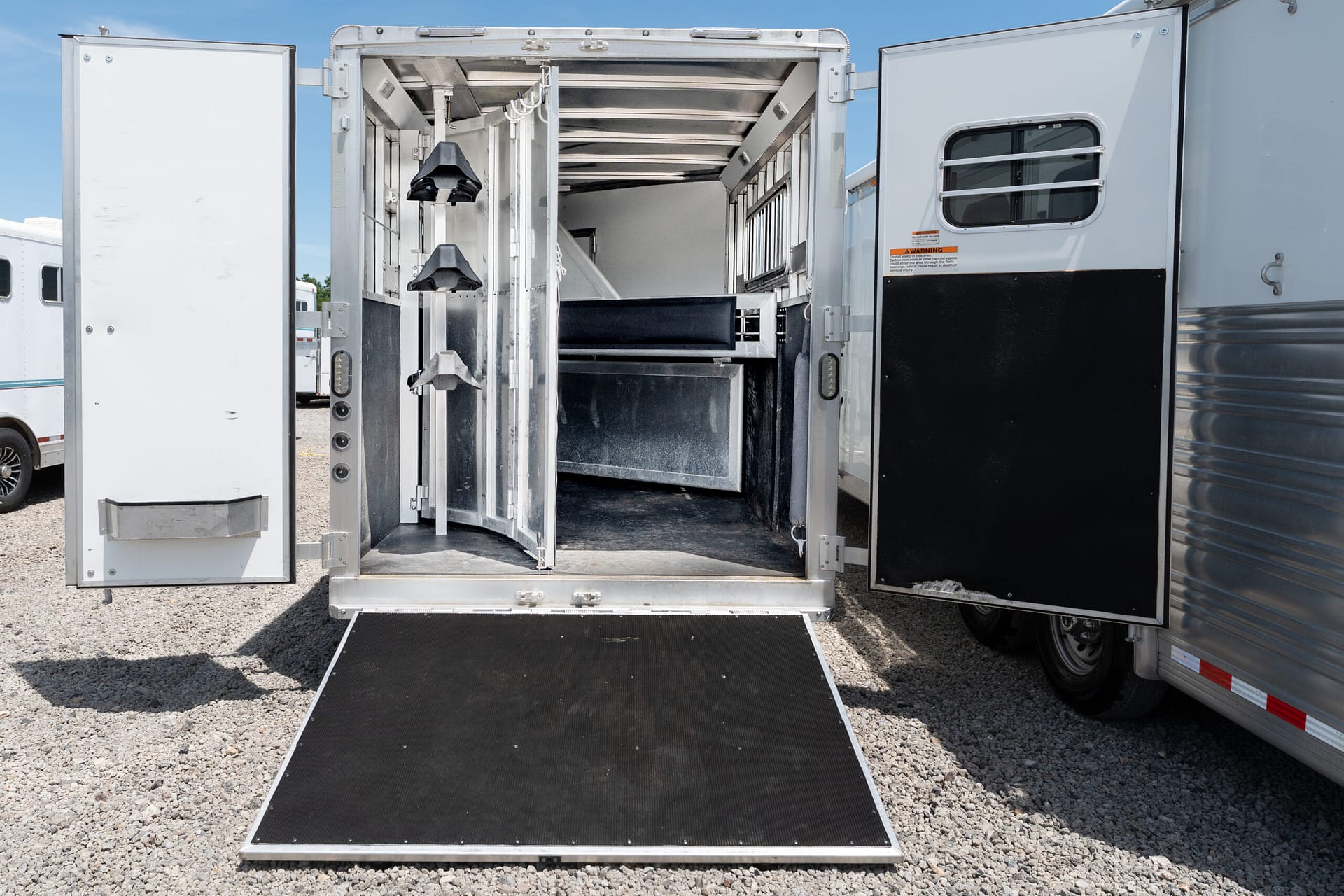 Open horse trailer with empty stalls and a ramp down to a gravel lot.