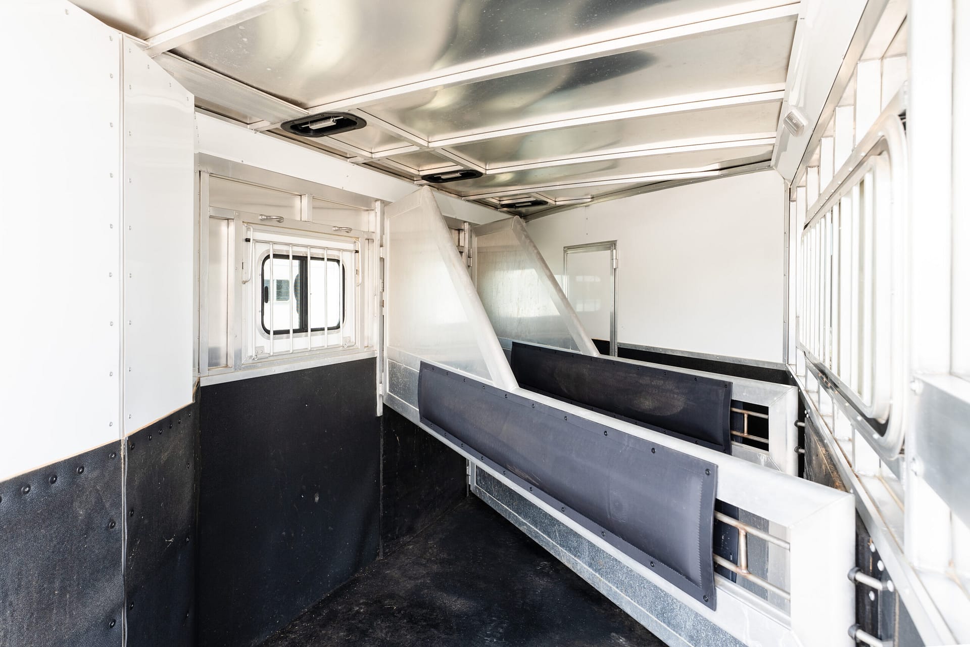 Interior of a metal livestock trailer with partition rails, barred window, and black non-slip floor.