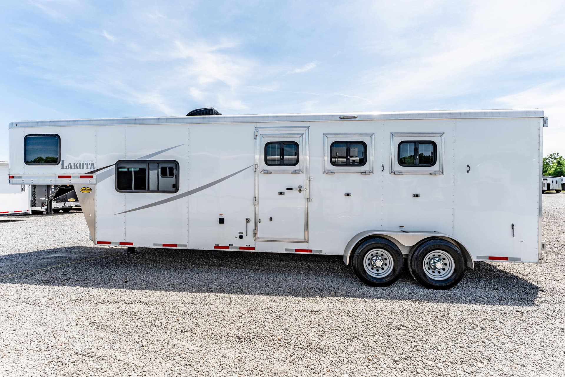 White Lakota horse trailer with two axles parked on gravel under a clear blue sky.