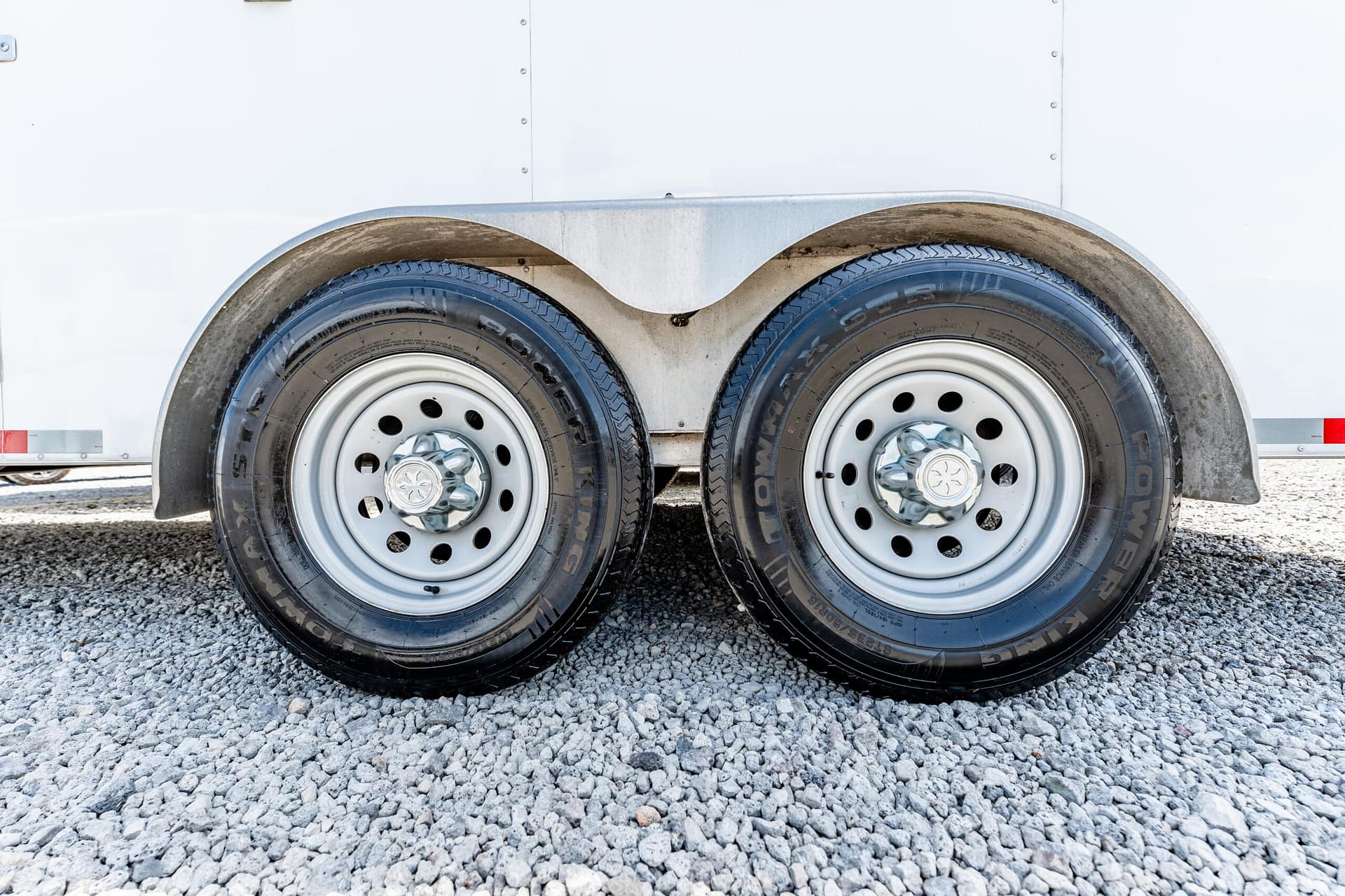 Close-up of two trailer wheels with curved metal fenders on a gravel surface down at ground level.
