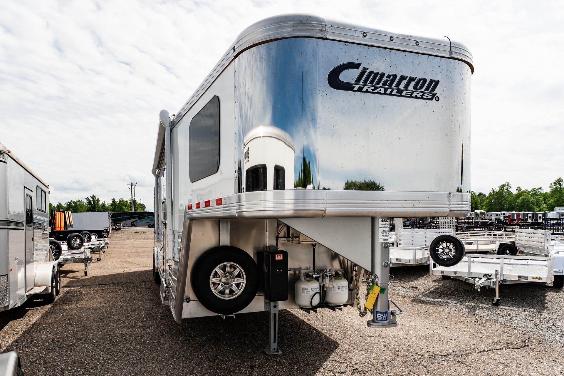 Polished aluminum Cimaron Trailers gooseneck trailer in a storage lot with other trailers nearby.