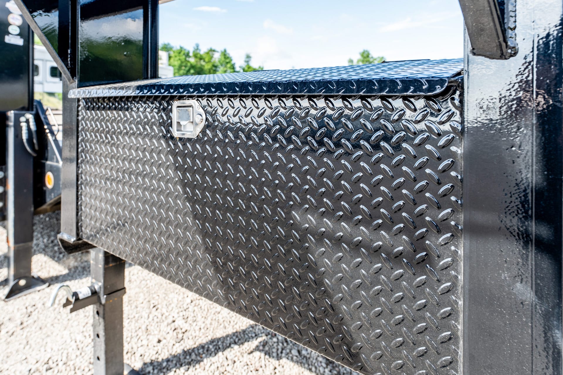 Diamond-plate metal stair tread on a trailer with a small latch handle in the foreground and a blue-sky background.