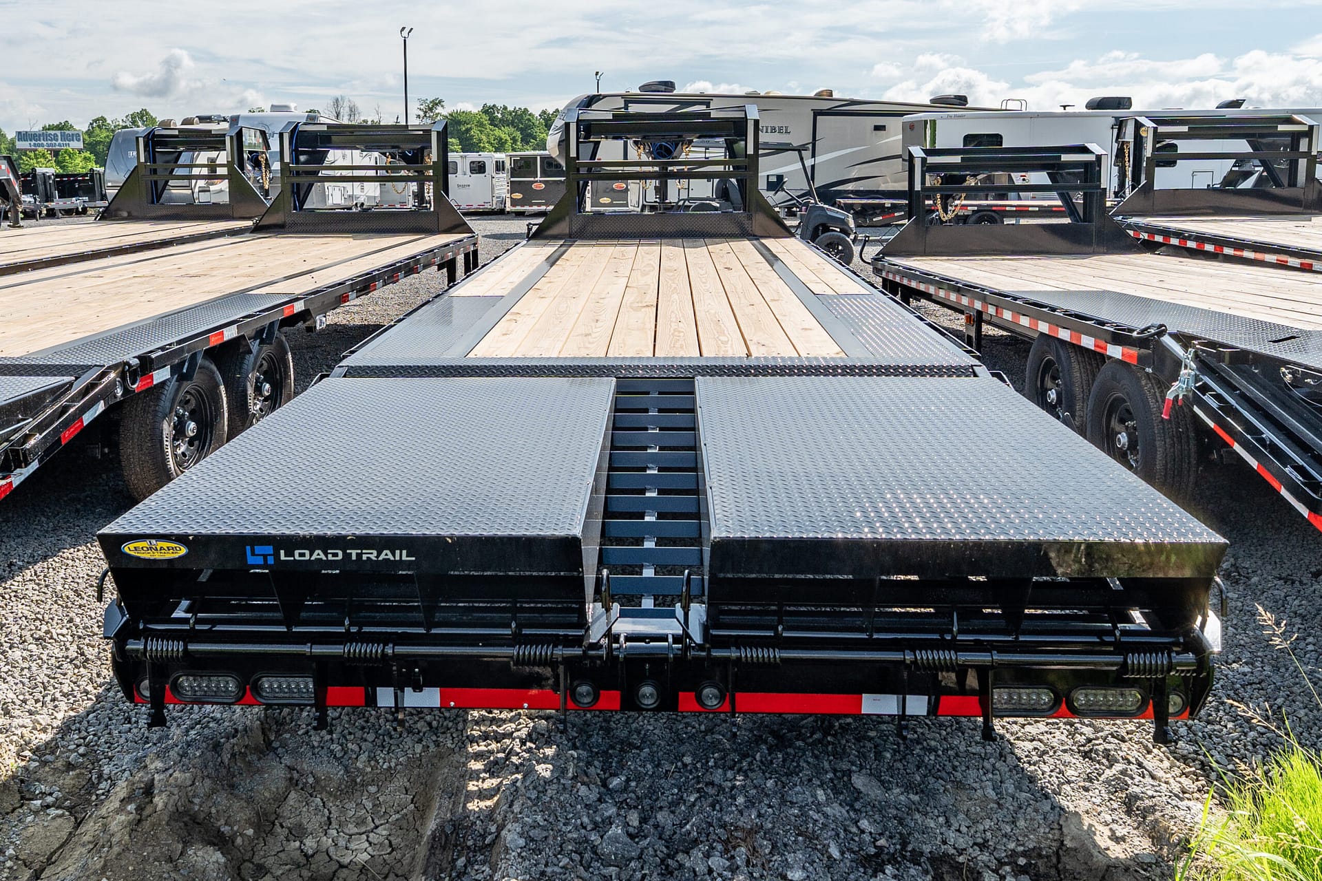 Flatbed trailers with wooden decks in a yard; a large hole is visible in the foreground next to the rigs.