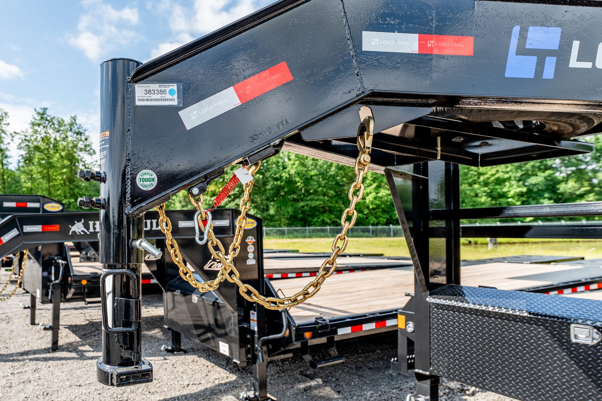 Close-up of a heavy-duty trailer hitch with gold safety chains hanging, outdoors on a sunny day.