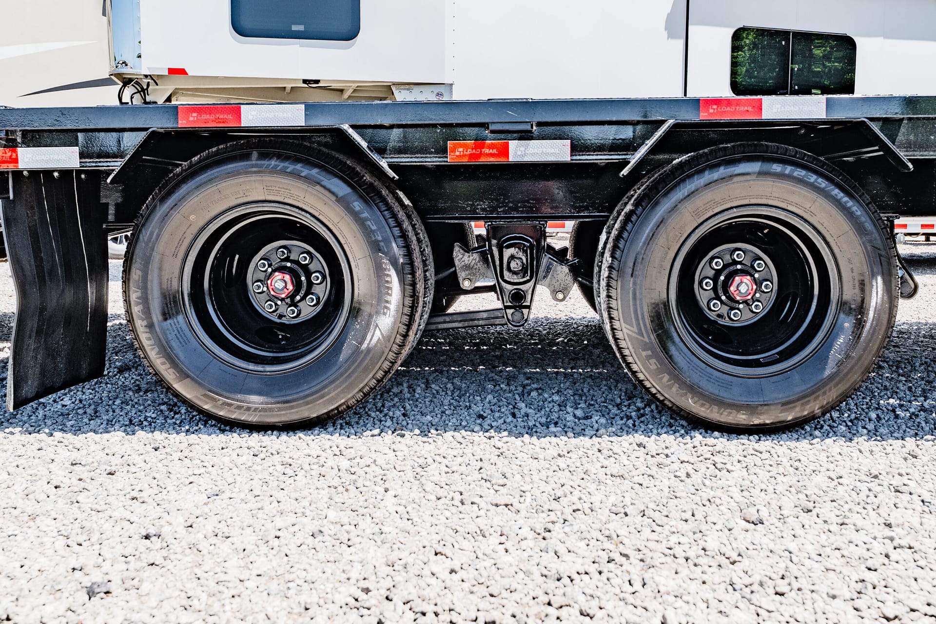 Close-up of dual trailer wheels and suspension undercarriage on a gravel surface on a heavy-duty trailer truck.