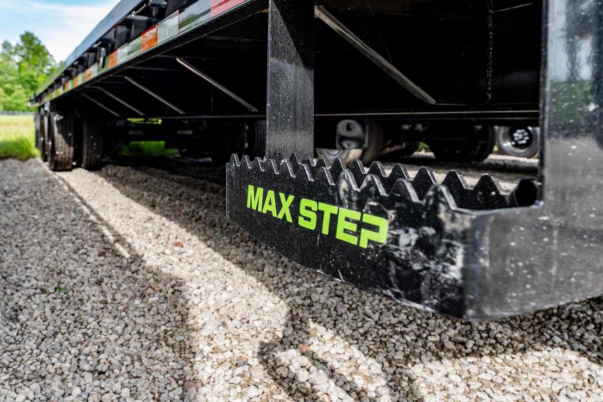 Close-up of a black trailer component with a serrated edge and bright green MAX STEER lettering on gravel ground.