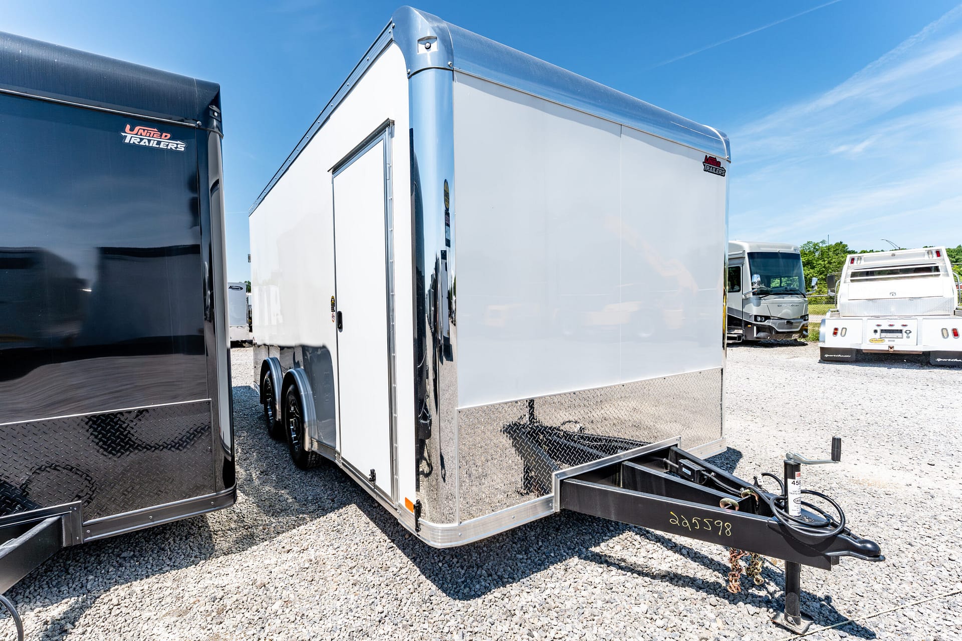 White enclosed cargo trailer with diamond plate ramp in foreground at a trailer lot under a blue sky.