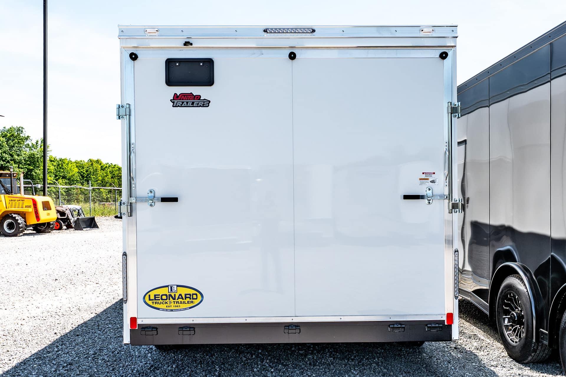 Rear view of a white trailer with a Leonard Truck & Trailer logo on the lower left, parked on gravel.