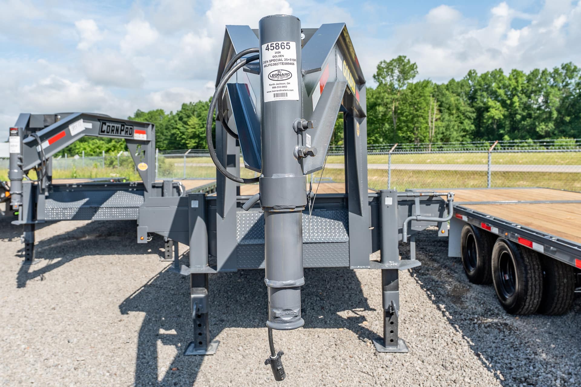 Close-up of a gray trailer jack and hitch on a flatbed trailer, with a coiled cable and label visible in the foreground.