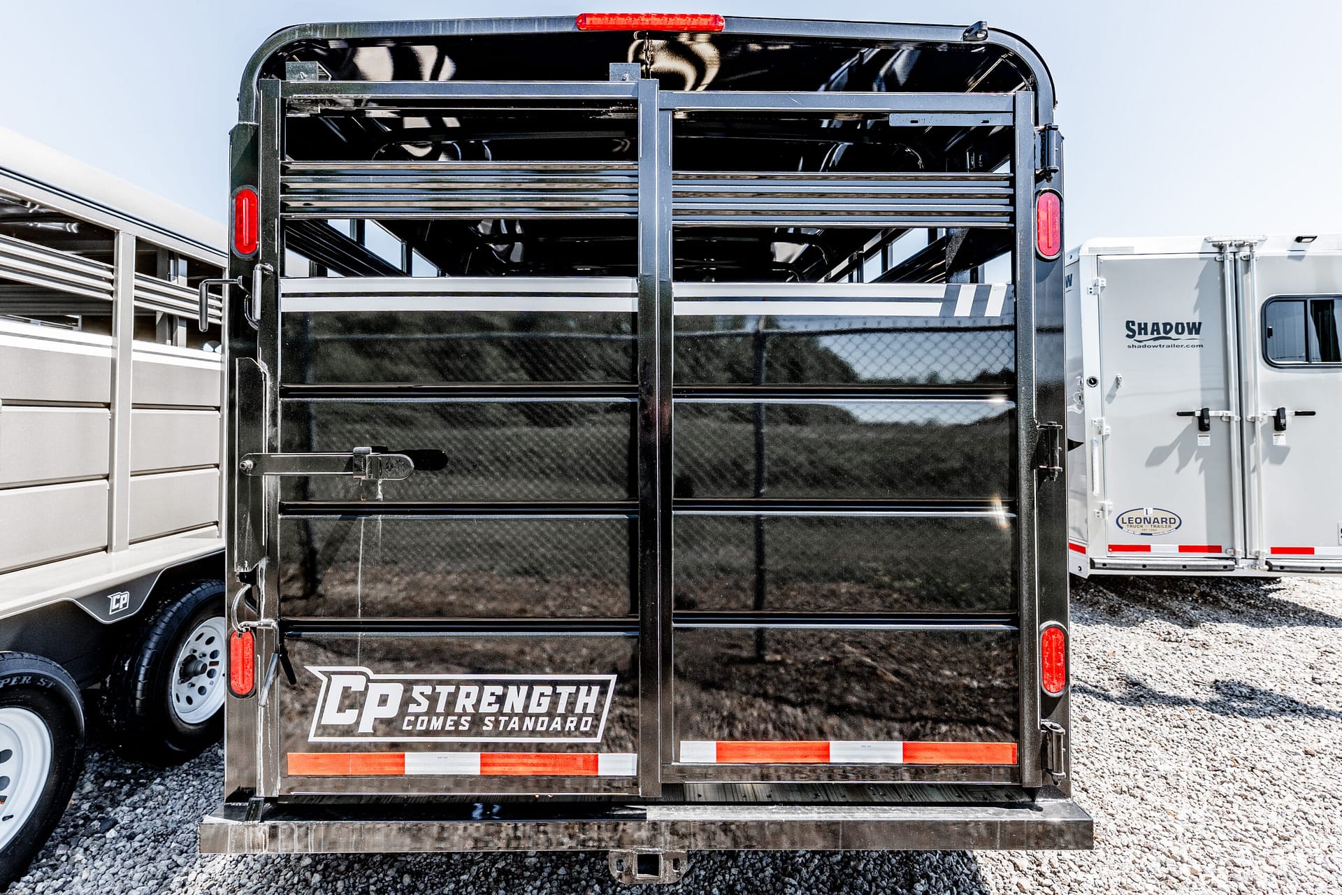 Rear view of a black metal trailer with slatted doors, red taillights, and the slogan 'C.P. STRENGTH COMES STANDARD' on the lower panel.