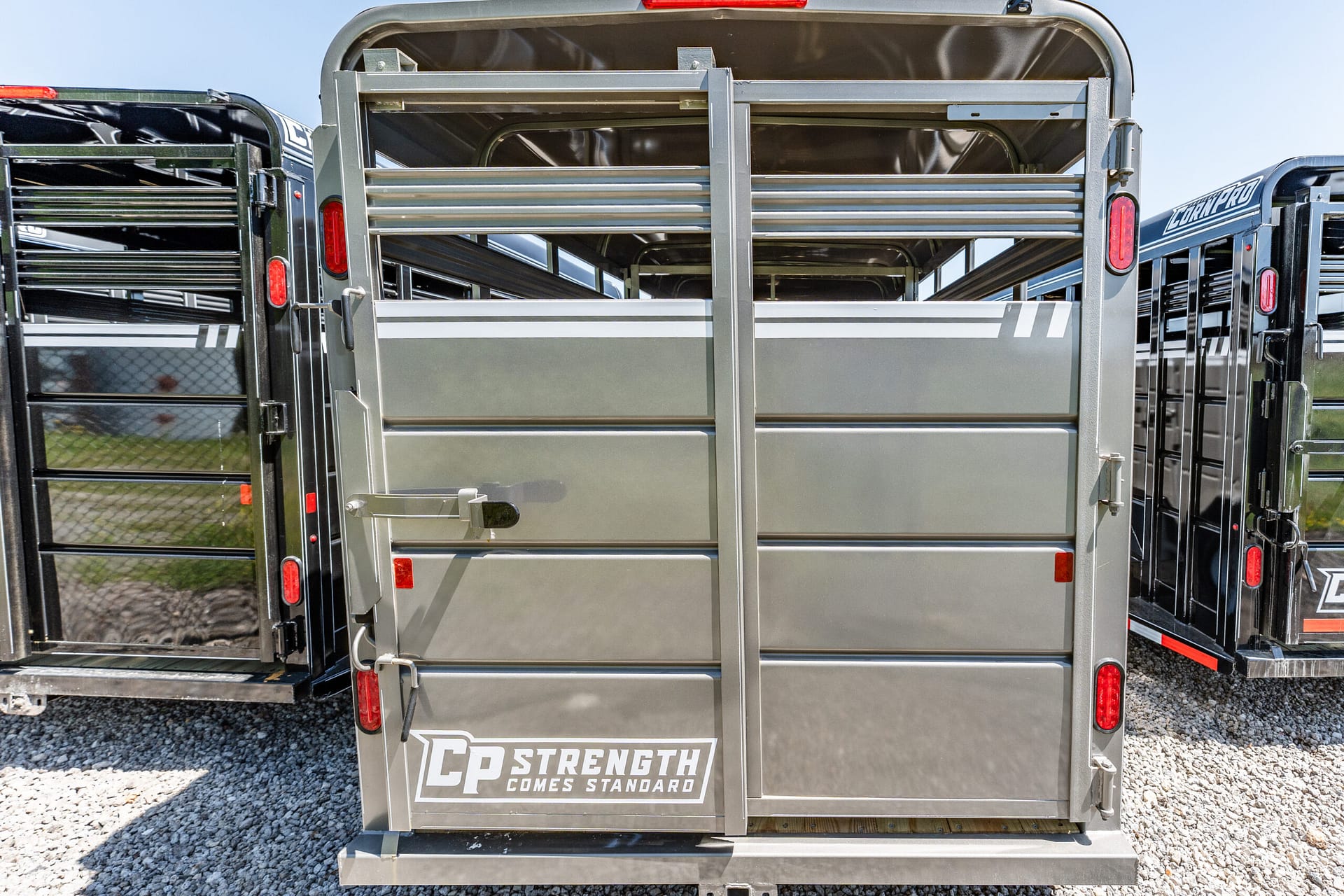 Rear view of a gray livestock trailer with metal gates, red taillights, and the slogan 'CP Strength Comes Standard' on the door frame.