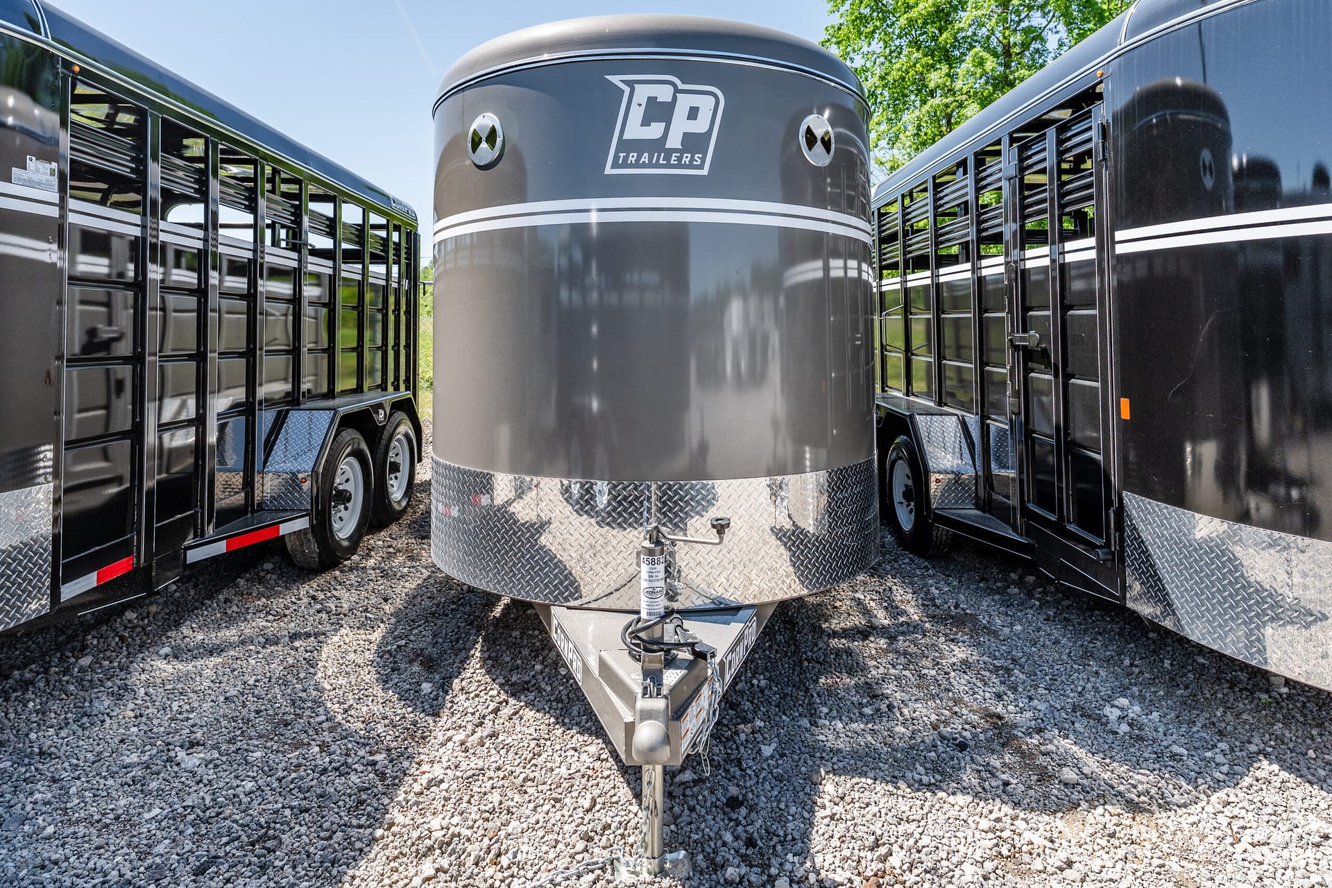 Front view of a large gray CP Trailers storage trailer between two other black trailers on a gravel lot, with a hitch in the foreground.