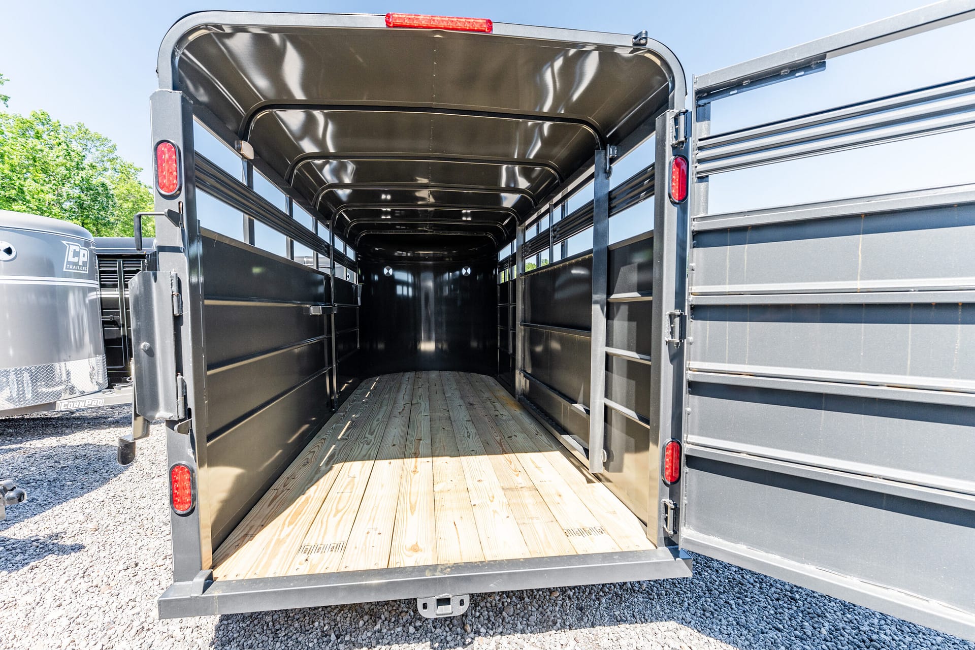 Open horse trailer interior with wooden floor and black metal walls, doors swung wide for loading relief light from outside.