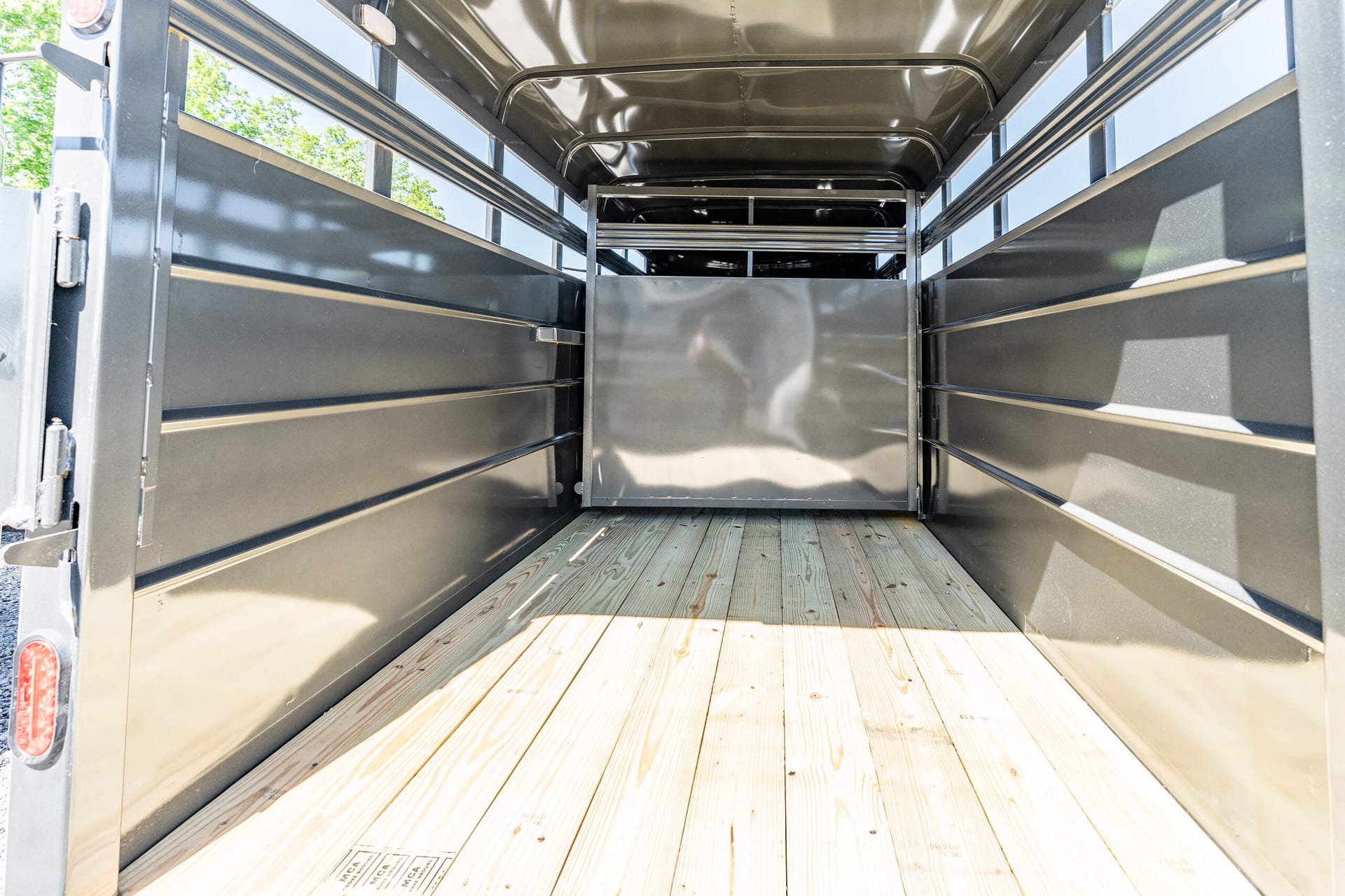 Empty metal cargo trailer interior with wooden planks on the floor and light entering from open rear doors.