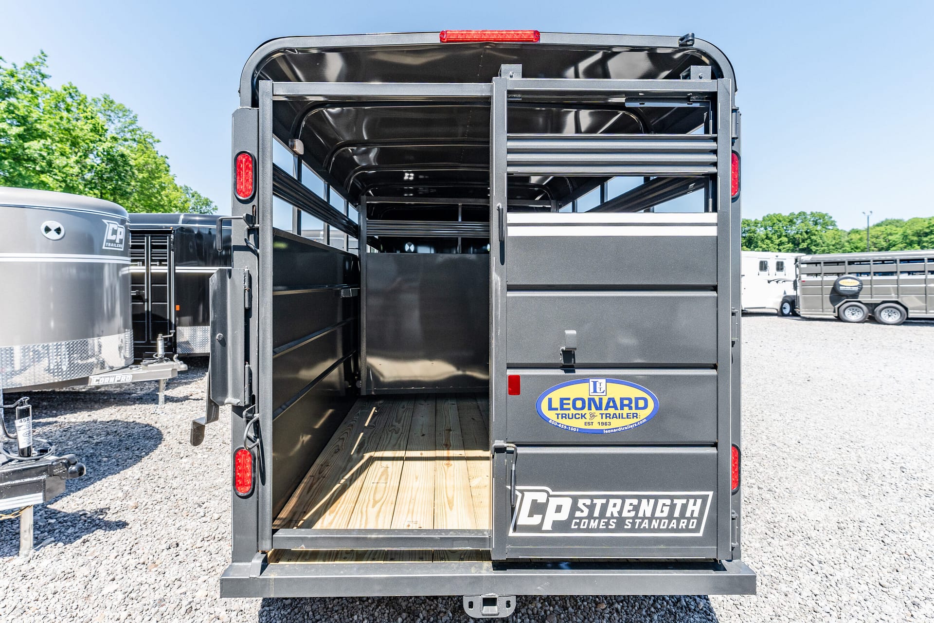 Rear view of a black livestock trailer with open doors and a wooden floor; Leonard Truck & Trailer logo on the back.