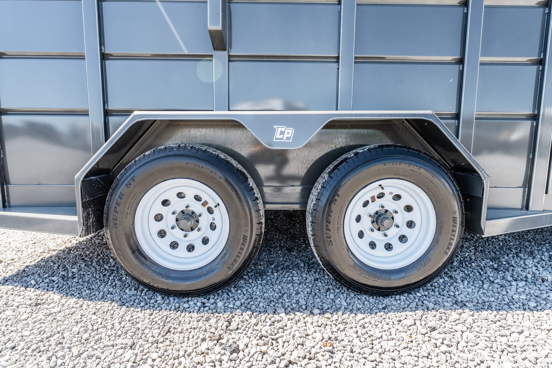 Dual-axle trailer wheels and fender with CP logo, gray metal side panels, parked on gravel ground