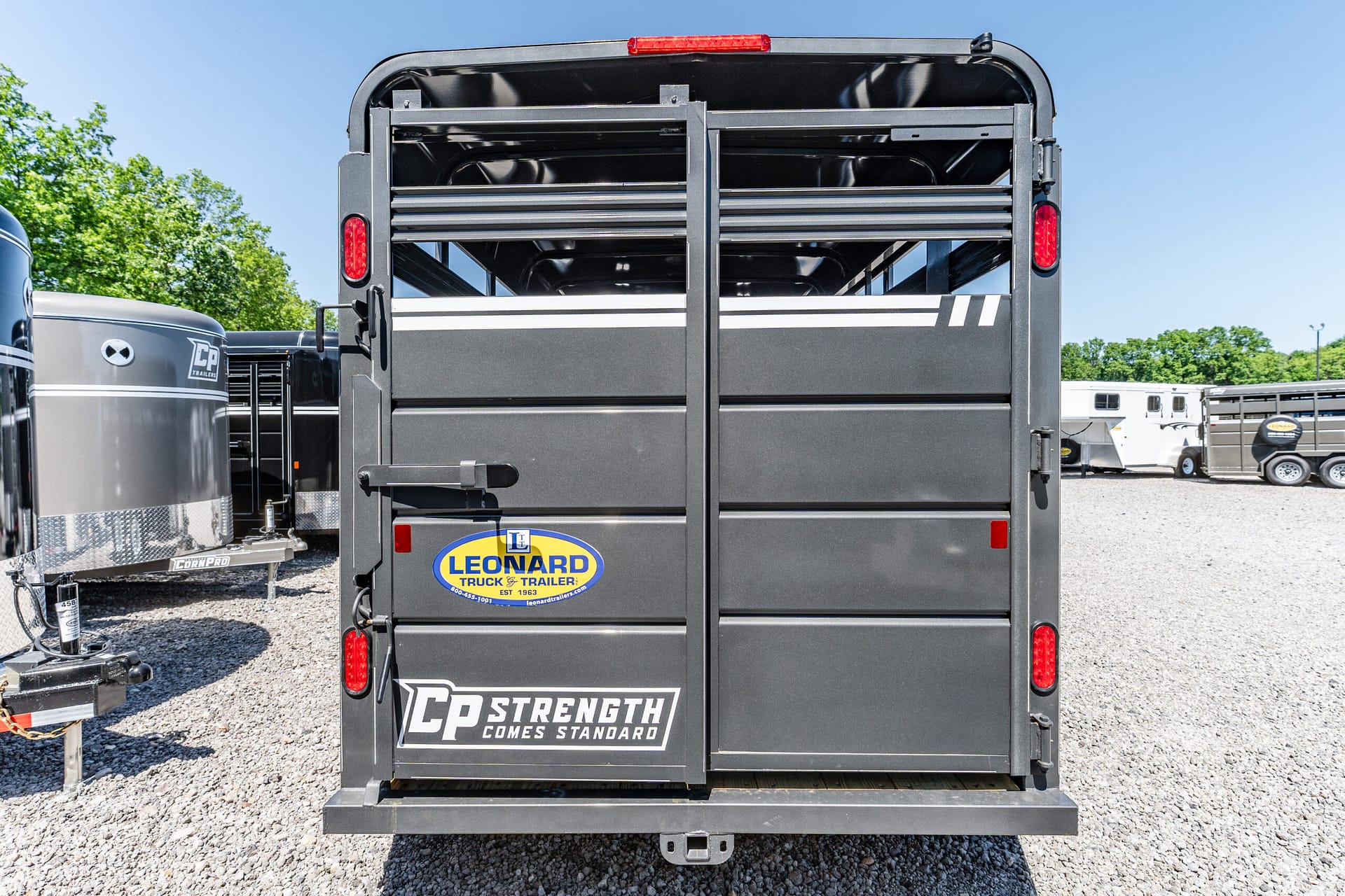 Rear view of a black trailer with silver horizontal slats, red taillights, and a Leonard Truck & Trailer sticker on the back.