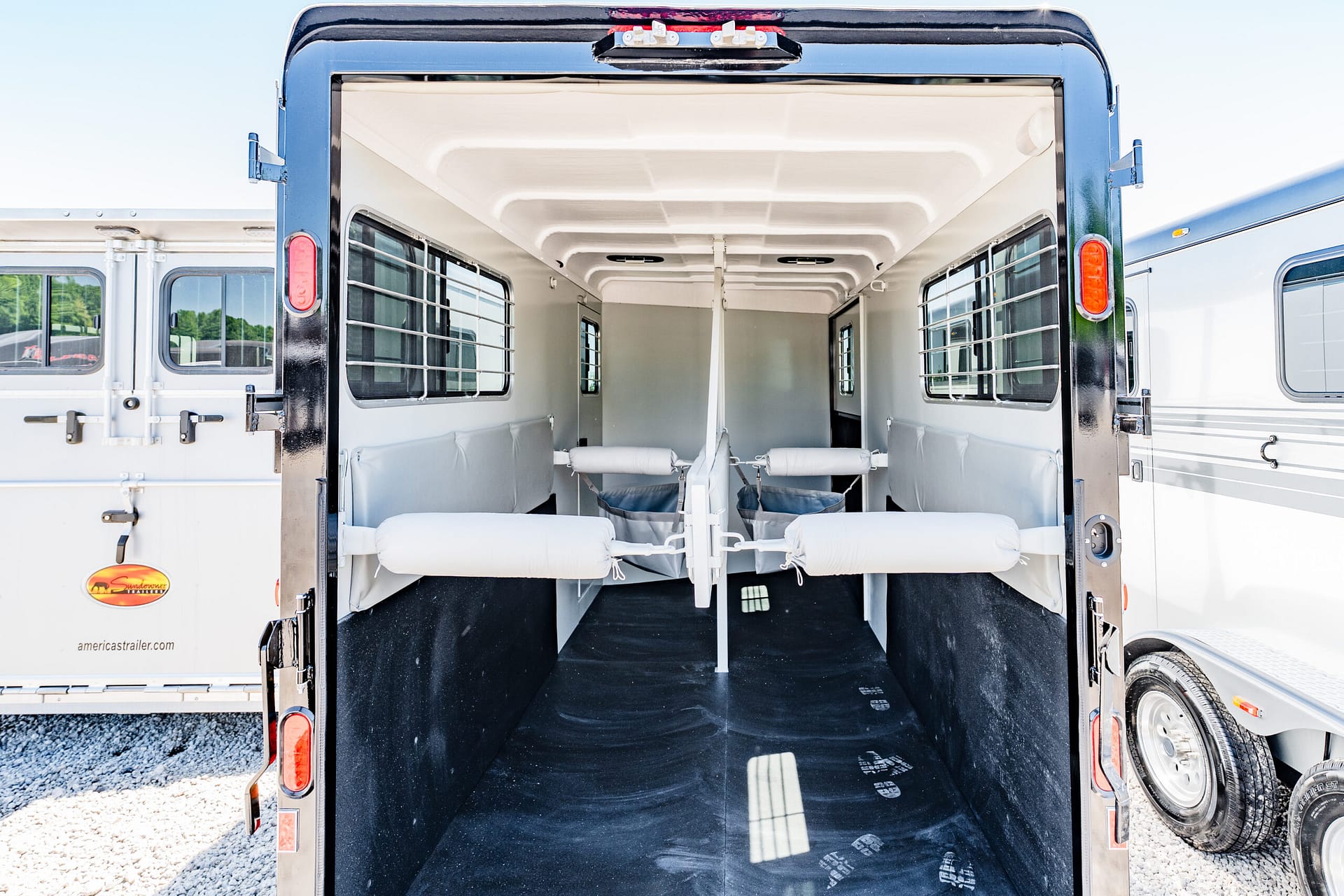 Interior of a horse trailer with padded stalls and partition rails seen through open rear doors