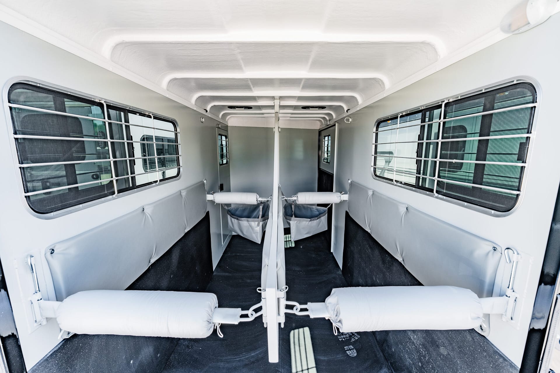Interior of a horse trailer with partitioned stalls, padded walls, and metal-barred side windows