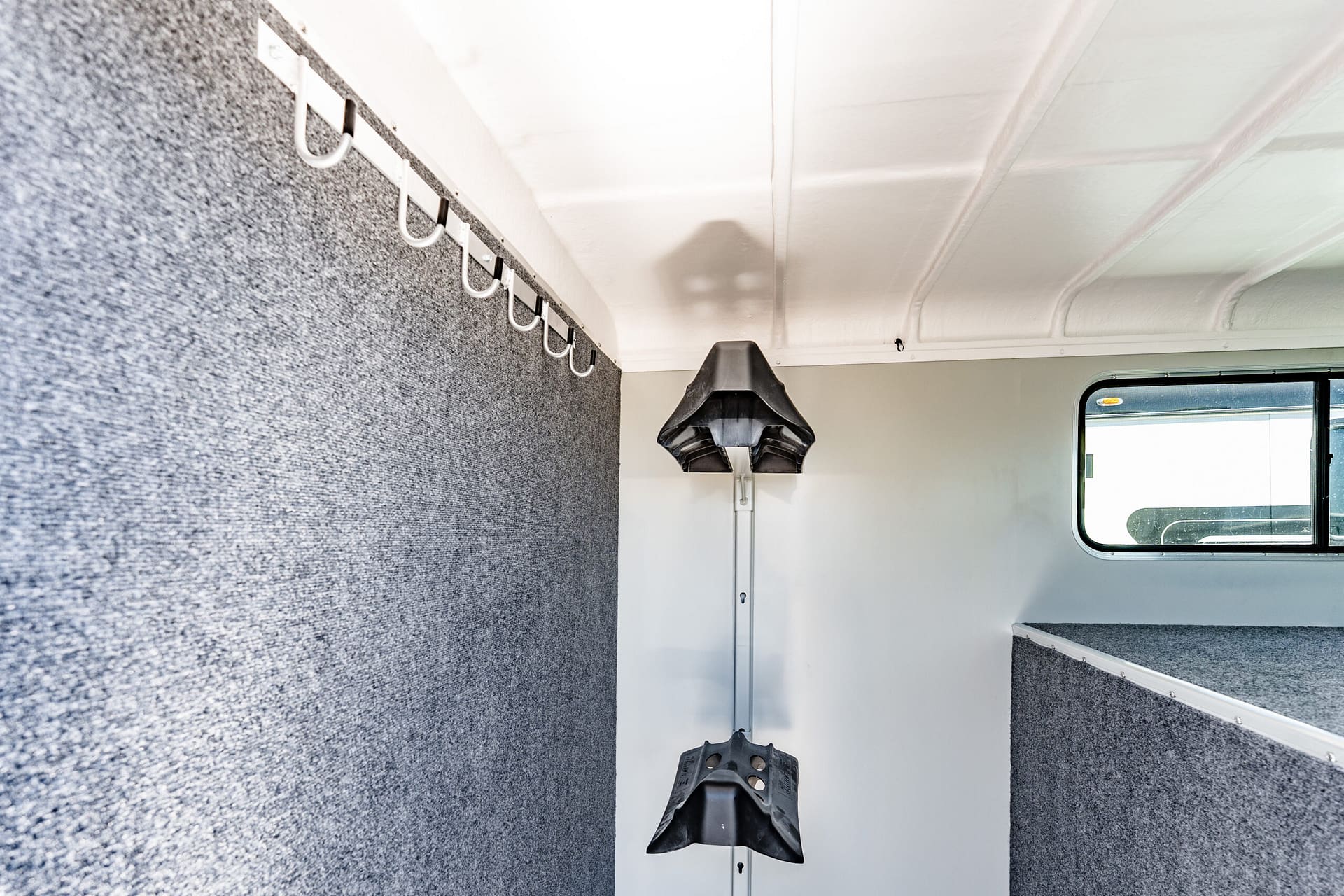 Interior of a vehicle with a row of white hooks mounted along a gray speckled wall and a window to the right